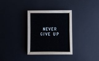 Inspirational letter board with 'Never Give Up' phrase on gray background.