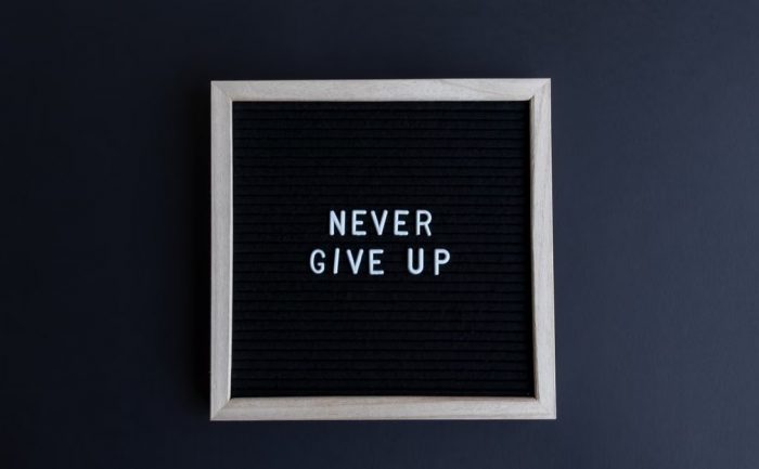 Inspirational letter board with 'Never Give Up' phrase on gray background.