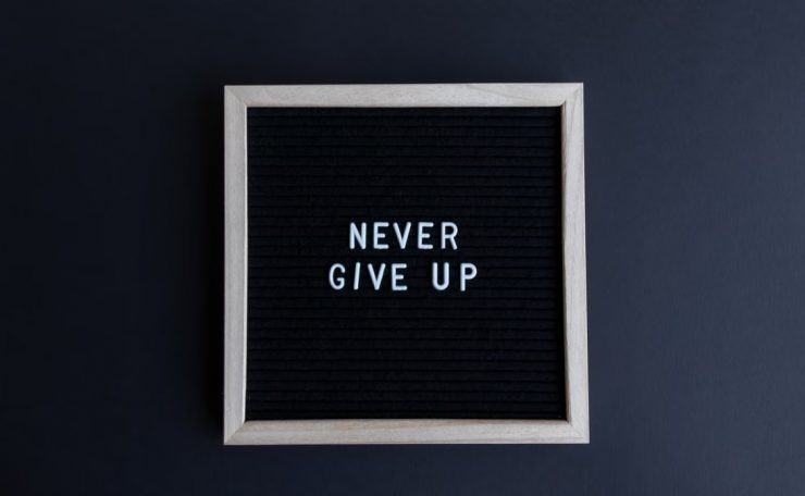 Inspirational letter board with 'Never Give Up' phrase on gray background.