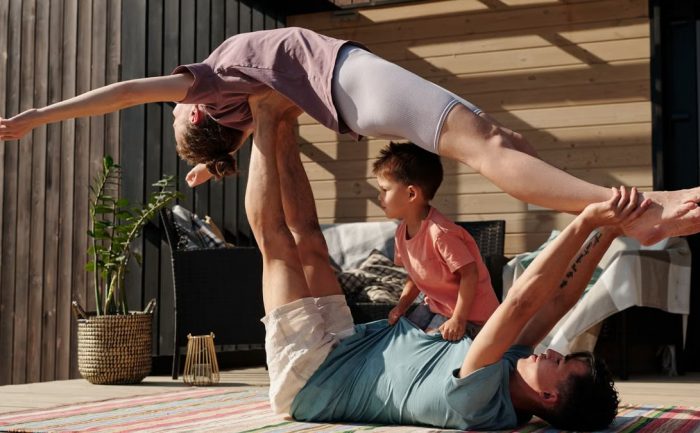 Father and kids doing yoga outdoors on a patio, balancing poses together.